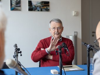 Three people are sitting at a table with microphones and conducting an interview indoors.