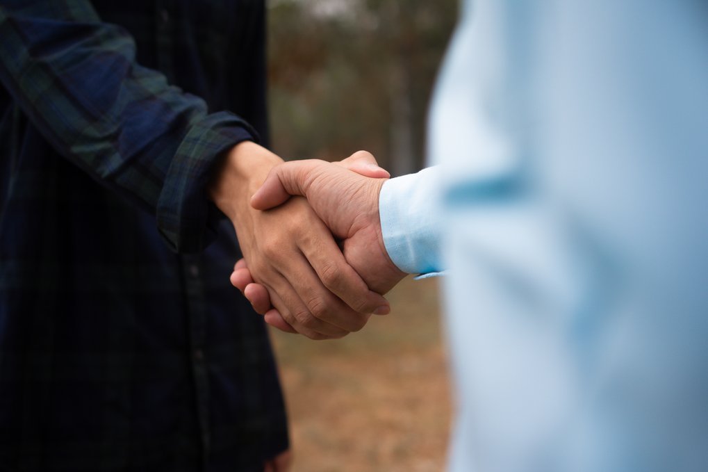 Zwei Personen schließen eine Vereinbarung durch Händedruck, Aufnahme fokussiert auf die Hände vor unscharfem Hintergrund.