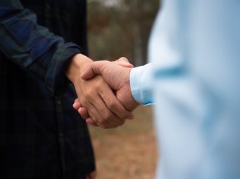 Zwei Personen schließen eine Vereinbarung durch Händedruck, Aufnahme fokussiert auf die Hände vor unscharfem Hintergrund.