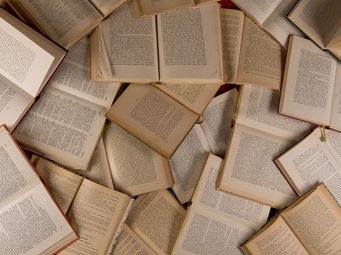 Zahlreiche geöffnete Bücher sind unregelmäßig auf einer Fläche verteilt und zeigen ihre Textseiten.