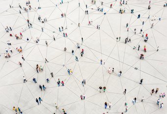 A large number of people are spread out across a vast square; they are connected to one another by a system of lines, forming a network.