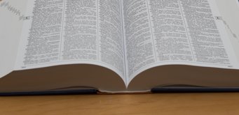Close-up of an open encyclopedia with text in multiple columns, placed on a wooden table.