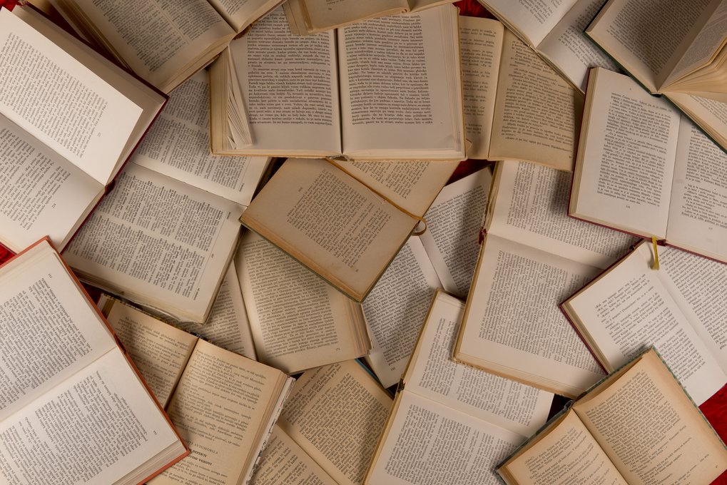 Zahlreiche geöffnete Bücher sind unregelmäßig auf einer Fläche verteilt und zeigen ihre Textseiten.