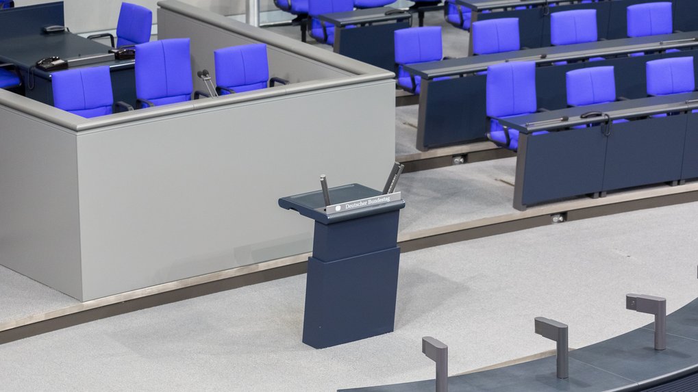 Rednerpult im Plenarsaal mit blauen Sitzen.