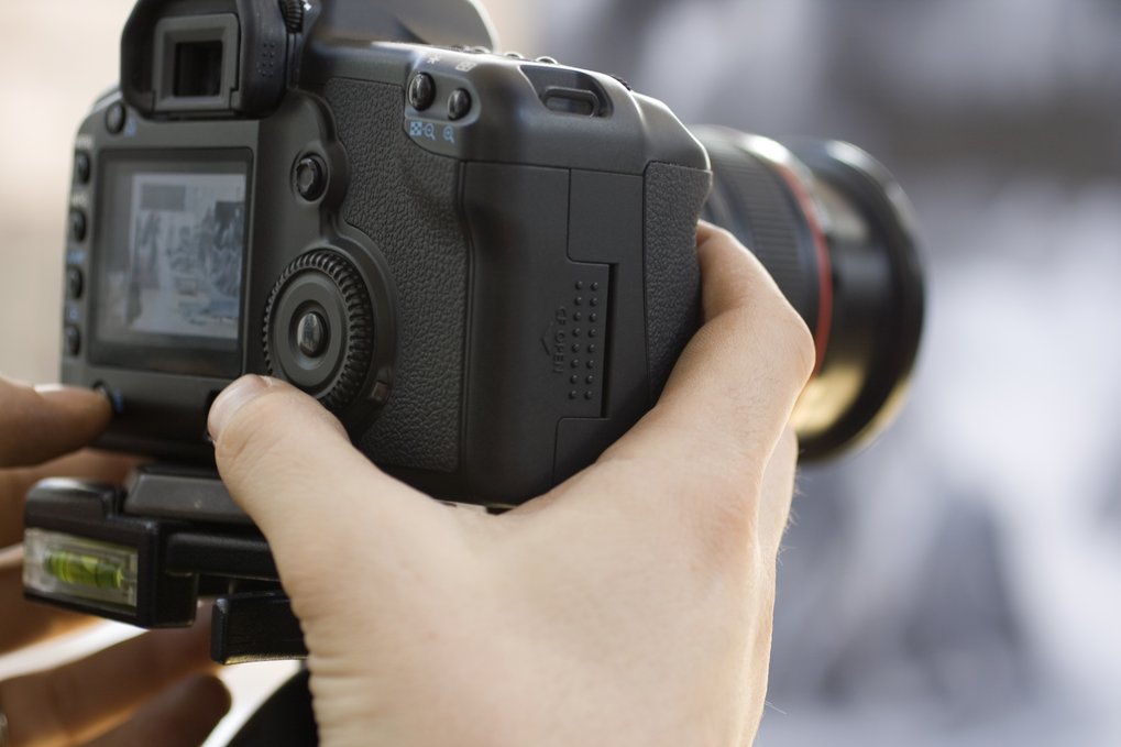Close-up of a hand adjusting a professional DSLR camera mounted on a tripod.