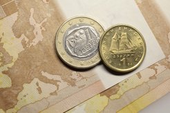 Zwei griechische Münzen, eine zeigt eine Eule auf einem Olivenzweig, die andere ein Segelschiff, liegen auf einer Europakarte.