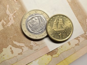 Zwei griechische Münzen, eine zeigt eine Eule auf einem Olivenzweig, die andere ein Segelschiff, liegen auf einer Europakarte.