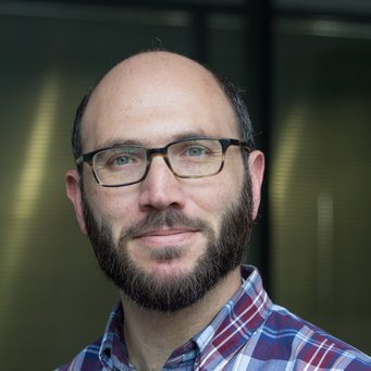 Bildbeschreibung (englisch) Person dressed in a red and blue plaid shirt, positioned indoors with a green background featuring vertical lines and soft lighting.