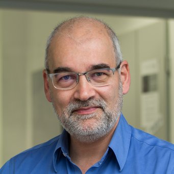 Ein Mann mit Bart und Brille, der ein blaues Hemd trägt, lächelt in die Kamera.