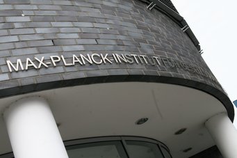 Das Bild zeigt den Eingang des Max-Planck-Instituts, dessen Name auf einer grauen Backsteinmauer zu sehen ist.