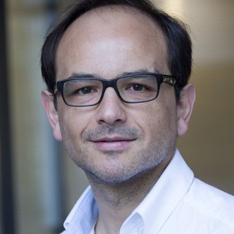 Matías Dewey Eine Person trägt ein weißes Hemd, das leicht geöffnet ist, und steht vor einem verschwommenen Hintergrund mit dunklem Haaransatz sichtbar.
