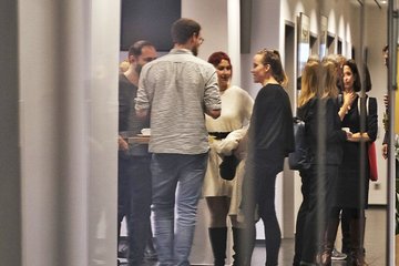 Das Bildmotiv zeigt mehrere Exemplare der Gattung Homo sapiens intellectualis stehend zu einer informellen Runde im Eingangsbereich des Instituts versammelt. Links im Bild ist ein Vorhang zu vermuten, der Blick auf die Runde wird durch spiegelhafte Verzerrungen etwas getrübt und lässt die Individuen teils leicht verschwommen erscheinen.