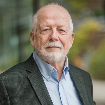 Fritz W. Scharpf Mann trägt dunklen Anzug und hellblaues Hemd, Hintergrund zeigt unscharfe Herbstbäume, moderne Glasarchitektur.