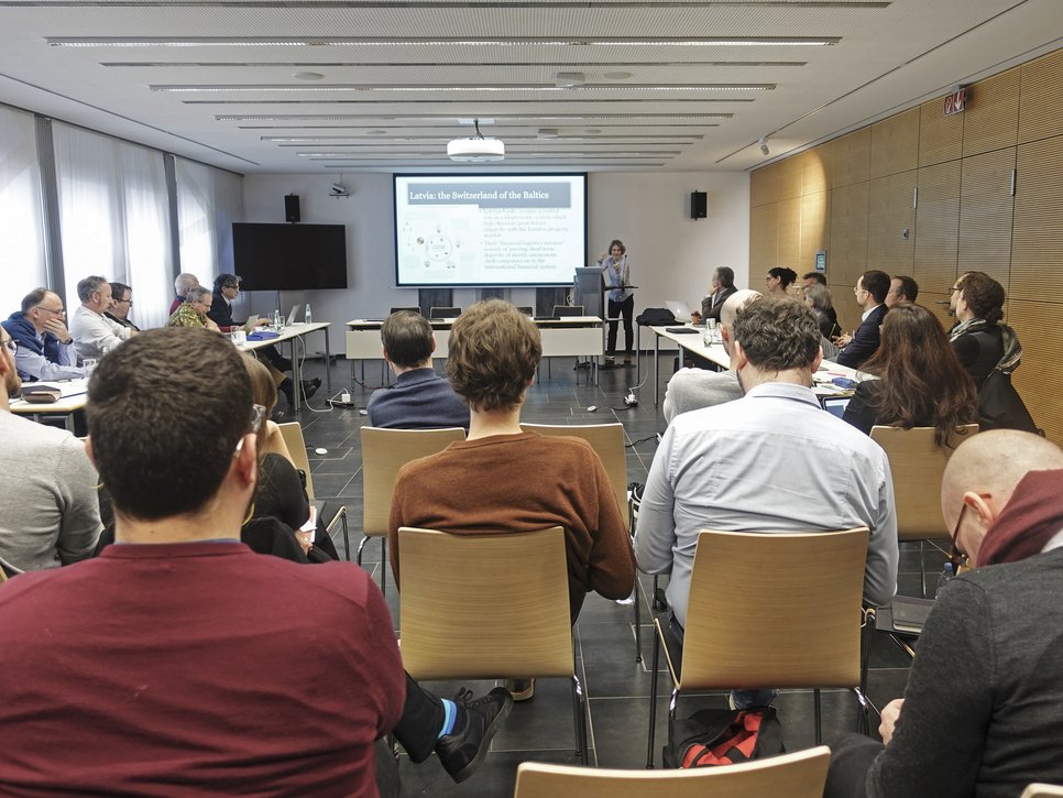 The photo provides a glimpse into a conference room where members of the species Homo sapiens intellectualis are seated at rectangular tables, following the event. In the background, an oversized monitor can be seen, presumably used for presentation purposes by the person in charge.