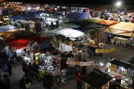 A vibrant night market with numerous stalls covered by colorful tents. Shoppers explore the diverse offerings under artificial lighting, creating a lively atmosphere.