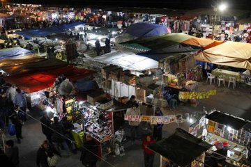 A vibrant night market with numerous stalls covered by colorful tents. Shoppers explore the diverse offerings under artificial lighting, creating a lively atmosphere.