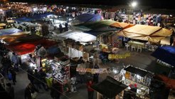 A vibrant night market with numerous stalls covered by colorful tents. Shoppers explore the diverse offerings under artificial lighting, creating a lively atmosphere.