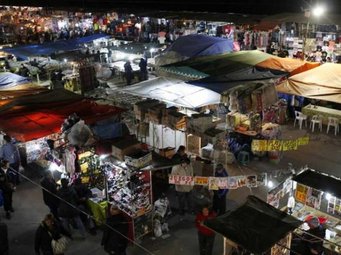 La Salada Market. Party of Lomas de Zamora. Great Buenos Aires Argentina. by Claudio Vallori. CC-BY-2.5 via Wikimedia Commons. A vibrant night market with numerous stalls covered by colorful tents. Shoppers explore the diverse offerings under artificial lighting, creating a lively atmosphere.