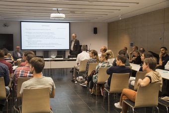 Akos Rona-Tas war im Jahr 2018 Scholar in Residence am MPIfG. Während seines Aufenthalts in Köln bot er die dreiteilige Vortragsreihe "Predicting the Future: From Augurs to Algorithms" an. Darin befasste er sich mit der Vorhersehbarkeit zukünftiger Ereignisse und dem Einsatz von Prognosen als strategische Instrumente. Ein Vortragender steht vor einem sitzenden Publikum, während im Hintergrund eine Präsentationsfolie mit Text zu sehen ist. Der Raum ist modern und gut beleuchtet.