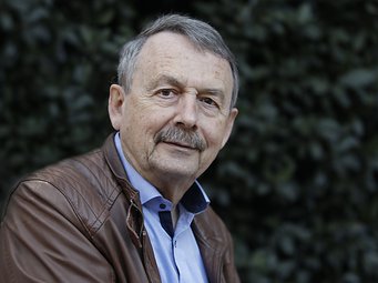 Wolfgang Streeck, Direktor emeritus am MPIfG Eine Person in einer braunen Lederjacke und einem blauen Hemd mit dunklem Kragen steht vor einem Hintergrund aus unscharfem Laub.