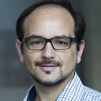 Matías Dewey A person is wearing a white shirt that is slightly open and is standing in front of a blurred background with dark hair visible.