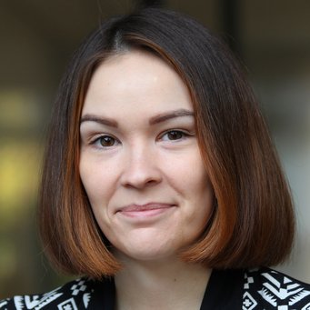 Kristina Gushchina A person with shoulder-length, dark brown hair in a bob cut can be seen in the photo. The jacket has a black and white geometric pattern. Blurred details are visible in the background.