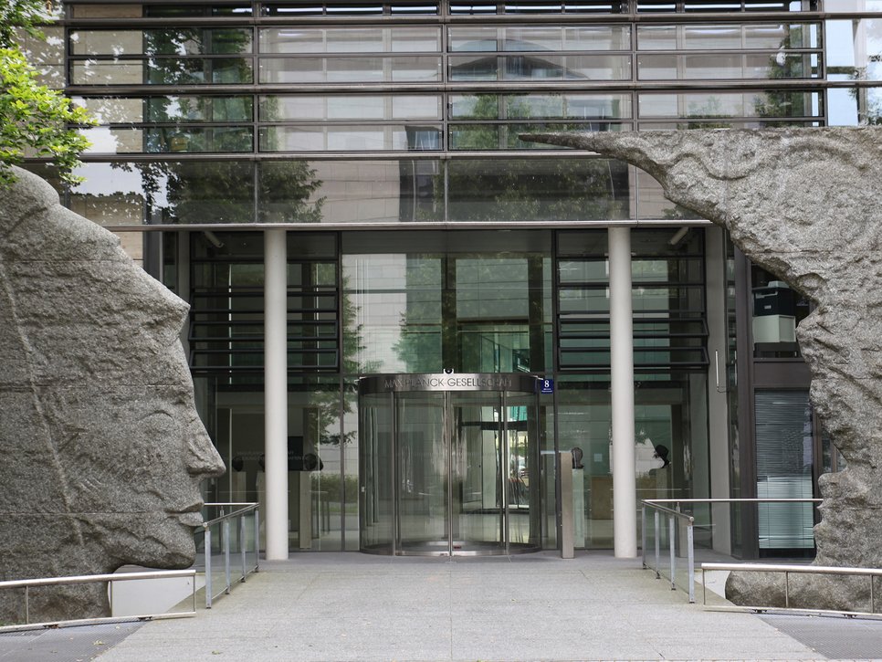 Moderne Glasfassade des Gebäudes der Max-Planck-Gesellschaft, flankiert von Steinskulpturen.