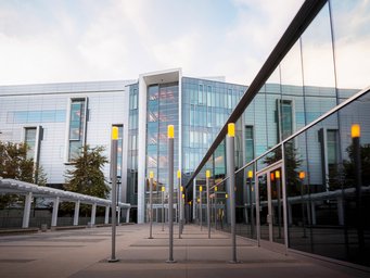 University of California, San Diego Large glass building facade with reflective windows, vertical yellow light bars in the entrance area, and surrounding trees.