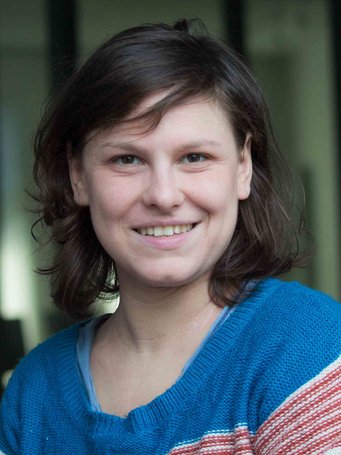 Alina Marktanner Person mit schulterlangem, dunkelbraunem Haar, trägt einen blauen Pullover mit roten und weißen Streifen im Ärmelbereich.
