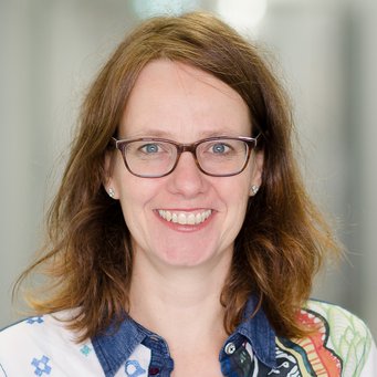 Simone Leiber Eine Person mit braunen Haaren, vermutlich weiblichen Geschlechts, trägt ein Hemd mit floralen und geometrischen Mustern sowie silberne Ohrringe. Der Hintergrund ist verschwommen.