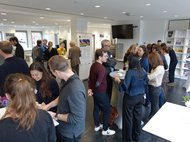 Mehrere Personen in kleinen Gruppen im Gespräch in einem Raum mit Stehtischen.