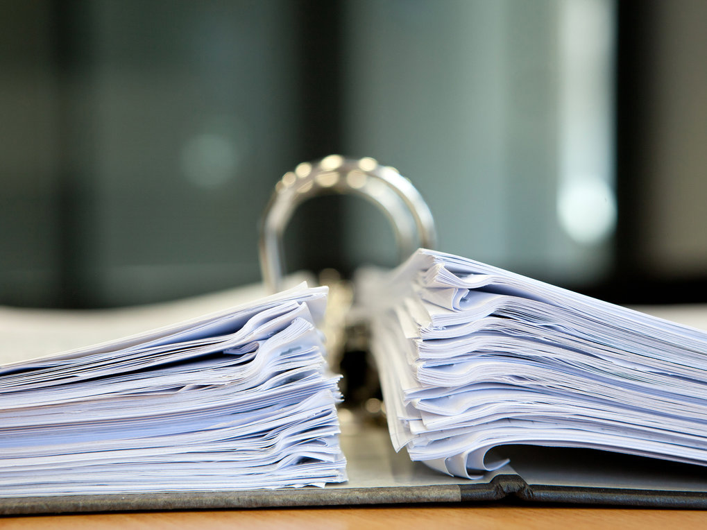 A close-up view of a large open binder filled with two thick stacks of paper, placed on a desk in a professional office environment.