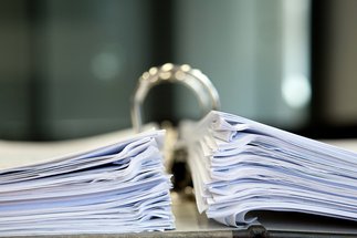 A close-up view of a large open binder filled with two thick stacks of paper, placed on a desk in a professional office environment.