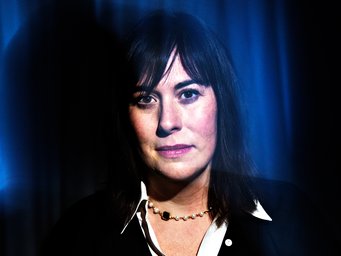 Brooke Harrington, Professorin für Soziologie, Dartmouth College, USA Schwarzes Haar fällt über die Schultern, eine elegante Perlenkette mit einem auffälligen dunklen Stein. Der Hintergrund ist dunkel, teils mit blauen Lichtstrahlen durchzogen. Bei der abgebildeten Person handelt es sich um die Sozialwissenschaftlerin Brooke Harrington.