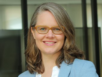 Das Foto zeigt Lisa Suckert, seit 2016 wissenschaftliche Mitarbeiterin am Max-Planck-Institut für Gesellschaftsforschung, die am 9. April 2024 von der Fakultät für Wirtschafts- und Sozialwissenschaften der Universität Hamburg habilitiert wurde. Eine Person mit schulterlangem braunen Haar, die einen hellblauen Blazer über einem weißen Hemd trägt, steht vor einer Glaswand.