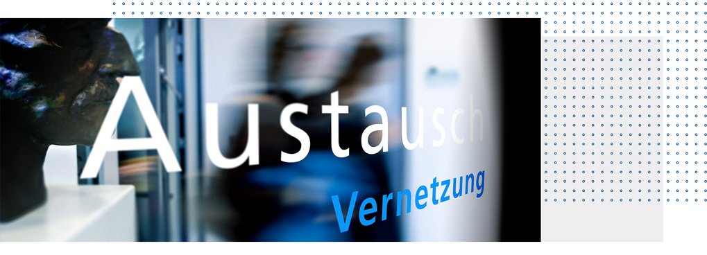 Der Schriftzug „Austausch Vernetzung“ auf einer Glasoberfläche, reflektiert im Vordergrund, während im Hintergrund eine unscharfe Person vorbeigeht. Ein dunkler Kopf einer Statue am linken Bildrand.