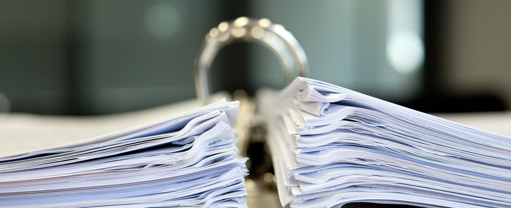 Nahaufnahme eines großen offenen Ordners, gefüllt mit zwei dicken Papierstapeln, der auf einem Schreibtisch in einer professionellen Büroumgebung steht.