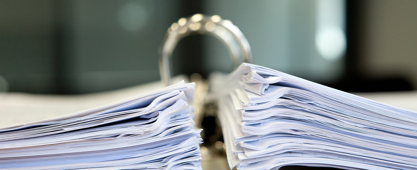 Nahaufnahme eines großen offenen Ordners, gefüllt mit zwei dicken Papierstapeln, der auf einem Schreibtisch in einer professionellen Büroumgebung steht.