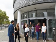 Eine Gruppe von Personen unterhält sich vor dem Eingang des Max-Planck-Instituts für Gesellschaftsforschung. Im Hintergrund ist eine Straße zu sehen.