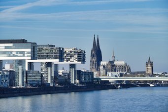 Kölner Skyline mit Dom und Kranhäusern Kranhäuser und der gotische Kölner Dom am Rheinufer, im Vordergrund der Rhein, am klaren Himmel mit wenigen Wolken.