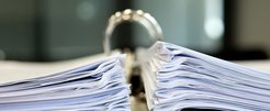 A close-up view of a large open binder filled with two thick stacks of paper, placed on a desk in a professional office environment.