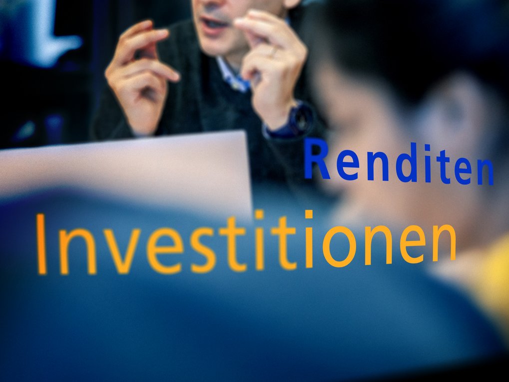 Unscharfe Fachleute in Diskussion mit großem gelbem Text „Investitionen” und kleinerem blauem Text „Gewinne” über dem Bild.