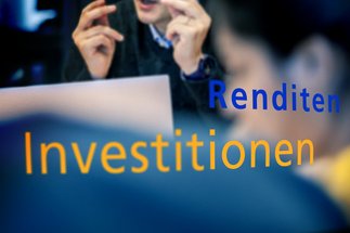 Unscharfe Fachleute in Diskussion mit großem gelbem Text „Investitionen” und kleinerem blauem Text „Gewinne” über dem Bild.