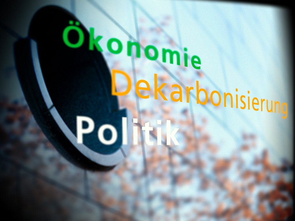 Begriffe Ökonomie, Dekarbonisierung und Politik, vor einem strukturierten Hintergrund mit verschwommenen Details.