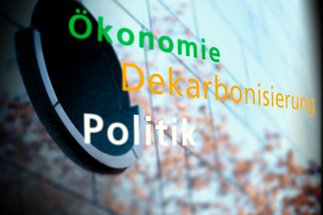 Begriffe Ökonomie, Dekarbonisierung und Politik, vor einem strukturierten Hintergrund mit verschwommenen Details.