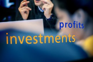 Blurred professionals in discussion with large yellow "investments" and smaller blue "profits" text overlaying the image.