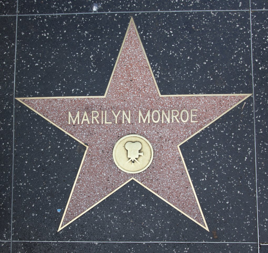 A pink terrazzo star on the Hollywood Walk of Fame honors Marilyn Monroe, with her name in gold lettering and a film camera symbol.