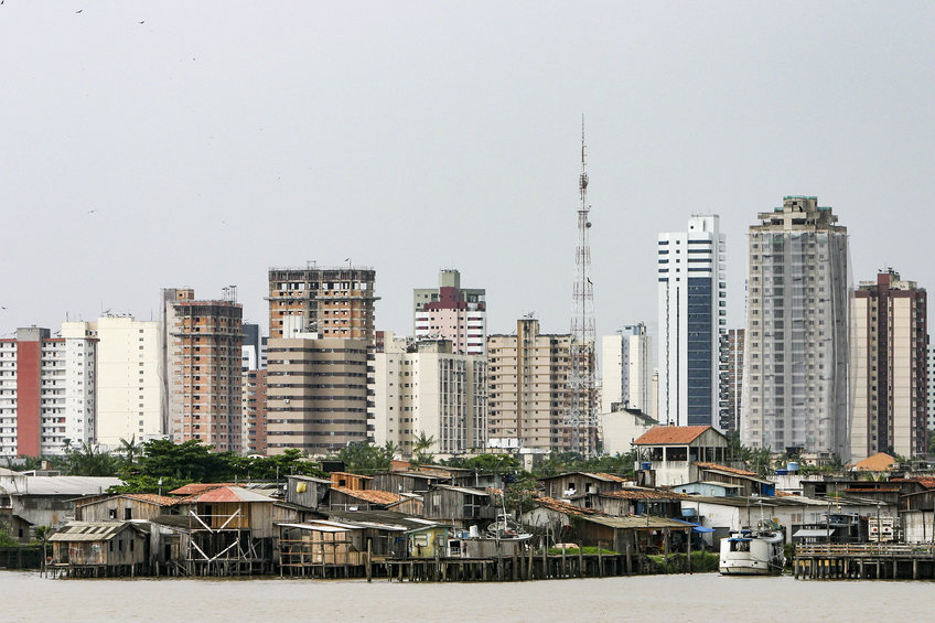 Stadtlandschaft mit modernen Hochhäusern und informellen Hütten Urban landscape featuring a mix of modern high-rise buildings and informal riverside shacks, with a prominent communication tower in the background.