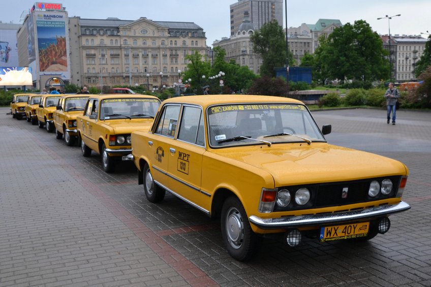 A line of yellow vintage taxis A line of yellow vintage taxis, each marked with "WPT 1313," parked on a paved city street, with historic architecture and green foliage visible in the background.