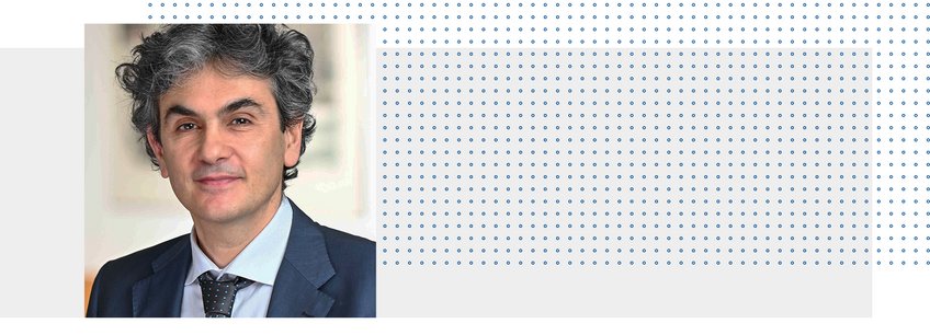 Prof. Dr. Lucio Baccaro Individual with curly hair, dressed in a dark suit against an abstract backdrop.